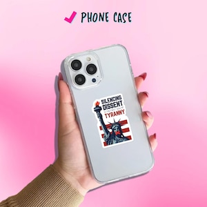 May include: Clear phone case with a sticker featuring the Statue of Liberty with a red band over her mouth and the text "SILENCING DISSENT IS THE FIRST SIGN OF TYRANNY". The phone case is labeled "PHONE CASE".