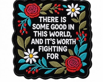 Może przedstawiać: Kwadratowa naszywka z haftem na czarnym tle z falistym brzegiem. Biały napis głosi: "THERE IS SOME GOOD IN THIS WORLD, AND IT'S WORTH FIGHTING FOR." Wokół znajdują się czerwone róże, białe stokrotki, zielone liście oraz czerwone jagody.