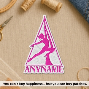 May include: A pink and white embroidered patch featuring a silhouette of a person performing aerial silks within a triangle. The text "ANYNAME" is below the figure. The patch is surrounded by sewing supplies.
