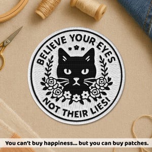 May include: Circular, white embroidered patch featuring the text "BELIEVE YOUR EYES NOT THEIR LIES!" around a black cat face with floral details. The patch has a white border.