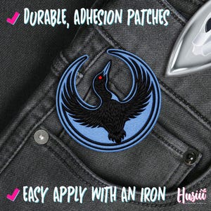 K&ouml;nnte beinhalten: Runder, gestickter Aufn&auml;her mit einem schwarzen Vogel mit roten Augen auf hellblauem Hintergrund. Der Aufn&auml;her befindet sich auf einer dunkelgrauen Jeans. Der Text auf dem Bild lautet "Durable, Adhesion Patches" und "Easy Apply With An Iron".