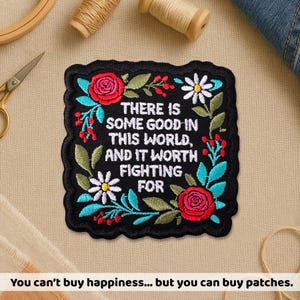 May include: Embroidered black patch with the quote "THERE IS SOME GOOD IN THIS WORLD, AND IT WORTH FIGHTING FOR." The patch is decorated with red roses, white daisies, and green leaves. The patch is square with a scalloped edge.