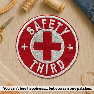 May include: A circular red and white embroidered patch with the text "SAFETY THIRD" and a white cross design. The patch has a white border. The text "You can't buy happiness... but you can buy patches" is at the bottom of the image.