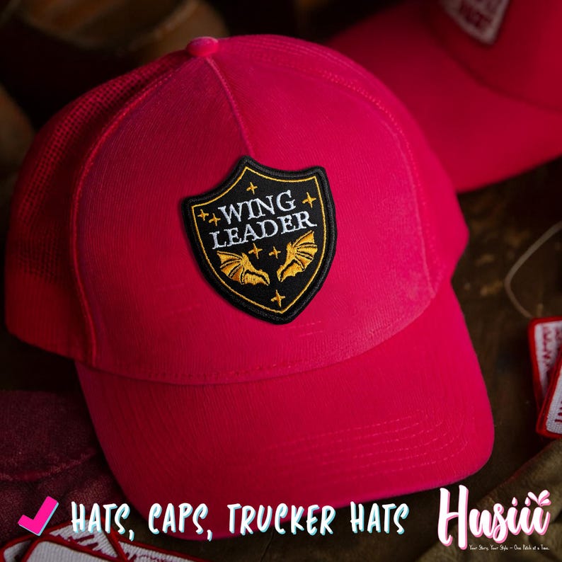 May include: A vibrant red trucker hat with a mesh back and a curved brim. The hat features a black and gold patch with the words "WING LEADER" and a bat design. The image also includes the text "HATS, CAPS, TRUCKER HATS".
