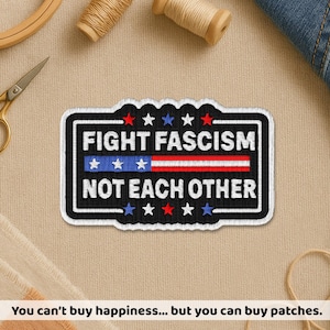 May include: Embroidered patch with the text "FIGHT FASCISM NOT EACH OTHER" in white on a black background. The design includes red and blue stars and stripes, resembling a flag. The patch is rectangular with a scalloped top edge.