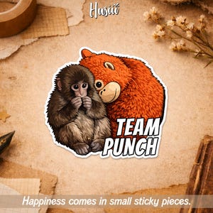 May include: A sticker featuring a cartoon illustration of a monkey and a bear hugging. The bear is orange, and the monkey is brown. The sticker has the words "TEAM PUNCH" in white block letters. The text "Happiness comes in small sticky pieces" is at the bottom.