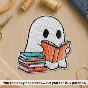 May include: Embroidered patch showing a white ghost reading an orange book, with a stack of colourful books. The ghost has black eyes and a black outline. The text at the bottom says, "You can't buy happiness... but you can buy patches."