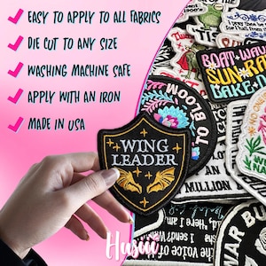 May include: A collection of embroidered patches, including a black and gold "Wing Leader" patch with bat wings. The image also shows patches with text like "Boat Wave Sun Ra Bake" and "To Bloom". The patches are easy to apply to all fabrics and made in the USA.