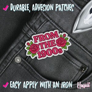 May include: An embroidered patch with the text "FROM THE 1900s" in pink, featuring red roses and green leaves. The patch is on a pair of dark gray jeans. The image also includes the text "DURABLE, ADHESION PATCHES" and "EASY APPLY WITH AN IRON".