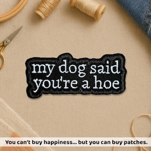 May include: Black embroidered patch with the text "my dog said you're a hoe" in white. The patch has a black border and is on a tan surface. Sewing supplies are in the background.