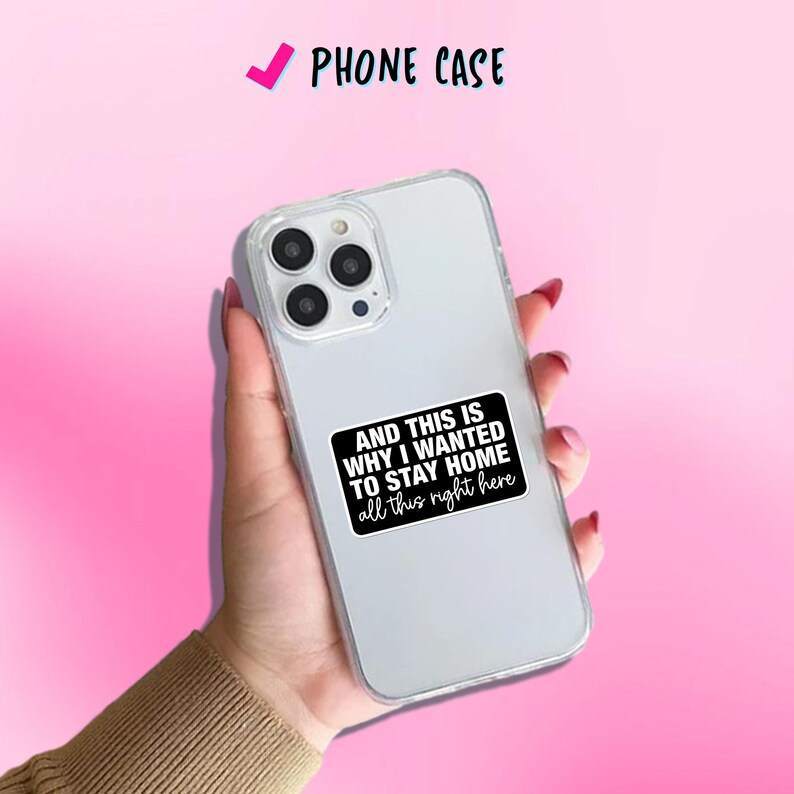 May include: Clear phone case with a black and white sticker that reads "AND THIS IS WHY I WANTED TO STAY HOME all this right here." The phone case is held in a hand against a pink background. The text "PHONE CASE" is at the top.