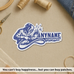 May include: A blue and white embroidered patch featuring a welder wearing a protective helmet and working with a welding torch. The design includes the text ANYNAME in bold capital letters to the right of the welder figure on a white background.
