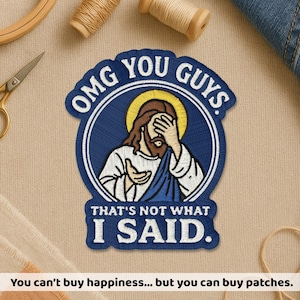 Peut inclure: Écusson brodé avec un motif de Jésus affligé et le texte "OMG YOU GUYS. THAT'S NOT WHAT I SAID." L'écusson est bleu, blanc et marron. Le bas de l'image indique "You can't buy happiness... but you can buy patches."