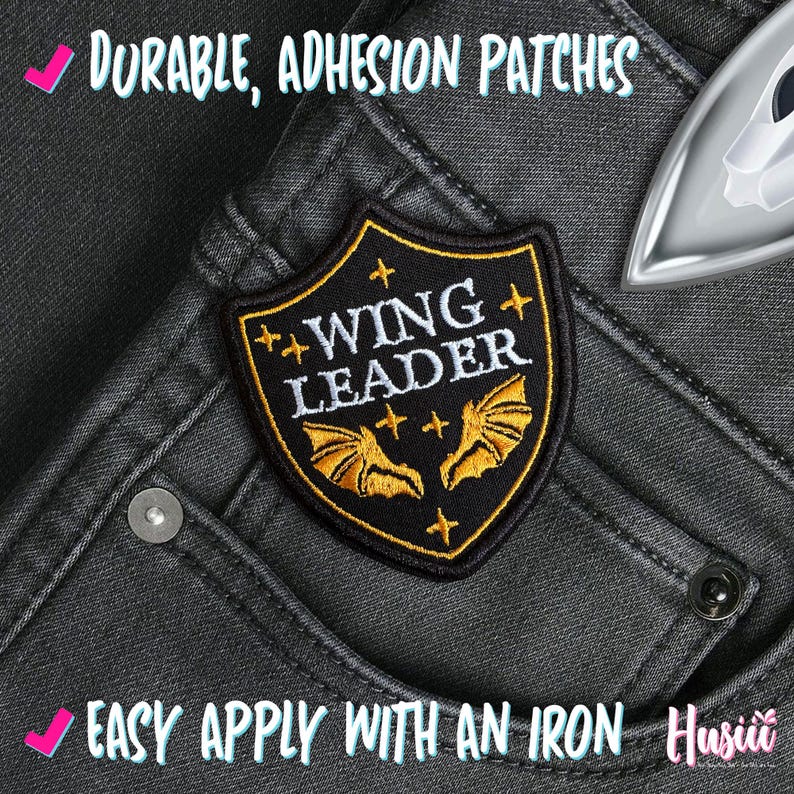 May include: A black and gold embroidered patch with the words "WING LEADER" and bat wings. The patch is on a pair of dark gray jeans. The text "DURABLE, ADHESION PATCHES" and "EASY APPLY WITH AN IRON" are also visible.