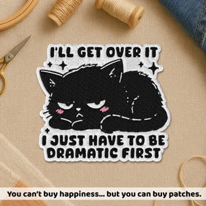 May include: Embroidered patch featuring a black cat with an annoyed expression, pink cheeks, and the text "I'LL GET OVER IT I JUST HAVE TO BE DRAMATIC FIRST." The patch is white with black text and a black cat design. The patch is likely for clothing or accessories.
