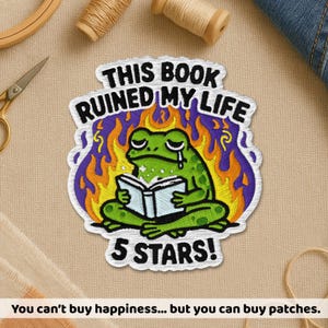May include: Embroidered patch featuring a green frog reading a book, with the text "THIS BOOK RUINED MY LIFE" and "5 STARS!". The frog is surrounded by flames. The patch is white with a purple border.