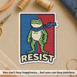May include: Embroidered patch featuring a green frog wearing a blue scarf, set against a red and blue background. The word "RESIST" is displayed in white block letters. The patch is surrounded by a white border.