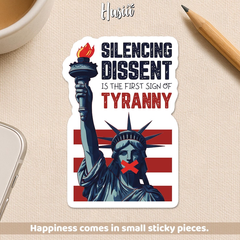 May include: A sticker featuring the Statue of Liberty with a red cross over her mouth and the text "SILENCING DISSENT IS THE FIRST SIGN OF TYRANNY." The sticker has a red, white, and blue color scheme, with the words in black and red.