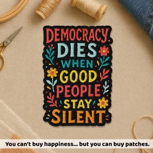 May include: A black embroidered patch with the text "DEMOCRACY DIES WHEN GOOD PEOPLE STAY SILENT" in colorful letters. The patch is decorated with floral and leaf designs. The bottom of the image reads "You can't buy happiness... but you can buy patches."