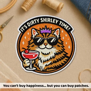May include: A circular embroidered patch featuring a brown tabby cat wearing black sunglasses and a purple crown. The cat holds a red cocktail with a cherry. The text IT'S DIRTY SHIRLEY TIME! is arched in black at the top against an orange background.