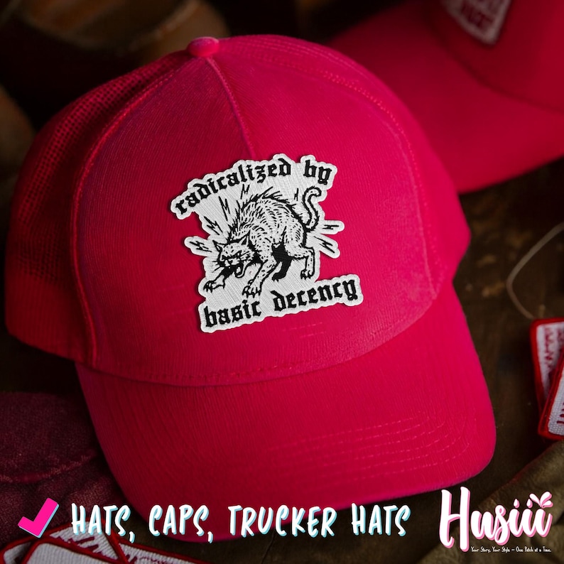 Peut inclure: Casquette de camionneur rose vif avec un dos en filet et une visi&egrave;re incurv&eacute;e. L'avant de la casquette pr&eacute;sente un &eacute;cusson avec une illustration de chat noir et blanc et le texte "radicalized by basic decency."