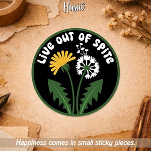 May include: A round sticker with a black background and a green border. The sticker features a yellow dandelion and a white dandelion. The text "LIVE OUT OF SPITE" is in white. The text "Happiness comes in small sticky pieces" is at the bottom.