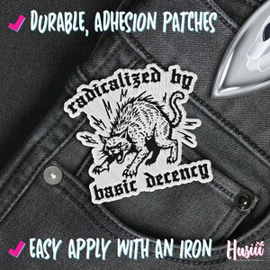 Peut inclure: &Eacute;cusson brod&eacute; avec une illustration en noir et blanc d'un chat en col&egrave;re, avec le texte "radicalized by basic decency". L'&eacute;cusson est sur un fond en jean gris. Le texte "Durable, Adhesion Patches" et "Easy Apply With An Iron" sont &eacute;galement visibles.