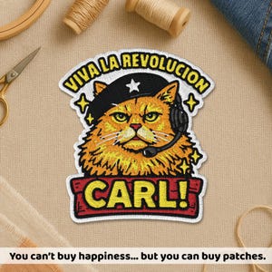May include: An embroidered patch featuring an orange cat wearing a black beret with a white star and a black headset. The text VIVA LA REVOLUCION is arched above the cat, and the name CARL! is printed in yellow on a red rectangular banner below.