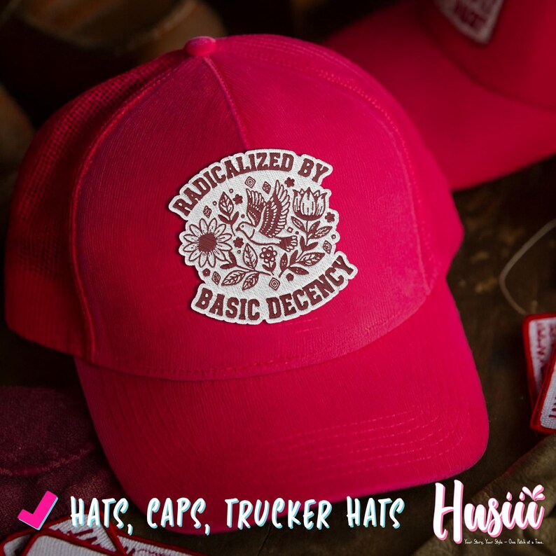 Peut inclure: Casquette de camionneur rouge vif avec un dos en filet et une visi&egrave;re incurv&eacute;e. Le chapeau pr&eacute;sente un &eacute;cusson blanc avec le texte "RADICALIZED BY BASIC DECENCY" entourant un motif floral et un oiseau. Le texte "HATS, CAPS, TRUCKER HATS" est &eacute;galement visible.