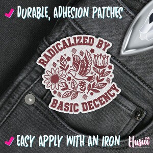 Peut inclure: Un &eacute;cusson thermocollant blanc et bordeaux avec le texte "RADICALIZED BY BASIC DECENCY" et des illustrations florales et d'oiseaux. L'&eacute;cusson est sur un jean gris fonc&eacute;. Le texte "DURABLE, ADHESION PATCHES" et "EASY APPLY WITH AN IRON" sont &eacute;galement visibles.