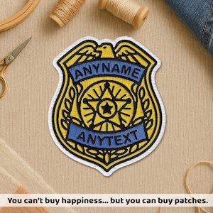May include: Embroidered patch in the shape of a police badge, featuring the text "ANYNAME" and "ANYTEXT" on blue banners. The badge has a yellow and black design with a star in the center. The text at the bottom says "You can't buy happiness... but you can buy patches."