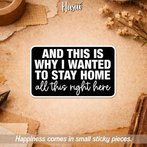 May include: A black sticker with white text that reads "AND THIS IS WHY I WANTED TO STAY HOME all this right here." The sticker is rectangular with rounded corners. The background is a textured, tan surface.