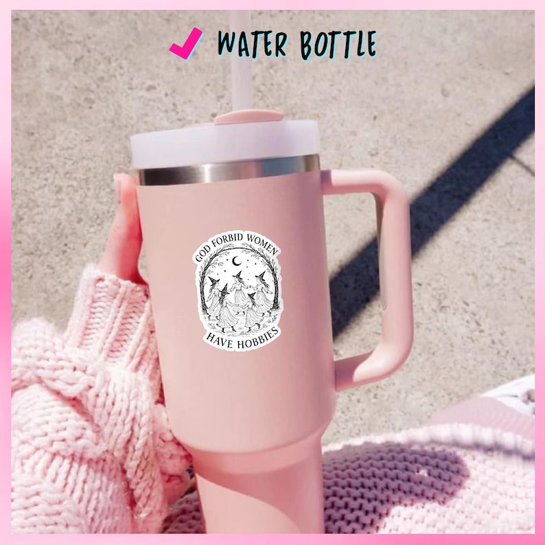 May include: A pink water bottle with a white lid and handle. The bottle has a sticker with the text "GOD FORBID WOMEN HAVE HOBBIES" and an illustration of witches. The words "WATER BOTTLE" are printed at the top.