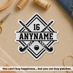 May include: An embroidered patch in white and black, featuring a hockey design. It includes crossed hockey sticks, a hockey ball, and the number 16. The text "ANYNAME" is displayed. The patch is set against a tan background.