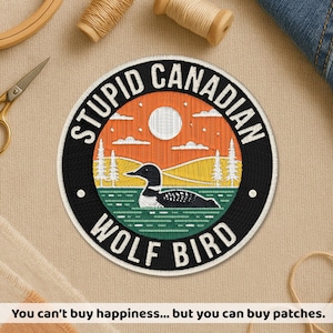 Peut inclure: Écusson brodé circulaire avec le texte "STUPID CANADIAN WOLF BIRD". Le motif comprend un huard sur un lac, un coucher de soleil et des arbres. L'écusson est noir, orange, blanc, vert et jaune.
