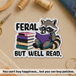 May include: Embroidered patch featuring a raccoon wearing glasses and reading a purple book, with a stack of books to the left. Text reads "FERAL BUT WELL READ." The patch is white with black, gray, and teal accents.
