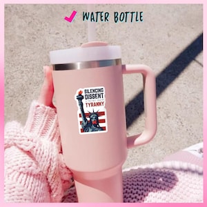 May include: A pink water bottle with a white lid and handle. A sticker on the bottle features the Statue of Liberty with a red band over its mouth and the text "Silencing Dissent is the First Sign of Tyranny."
