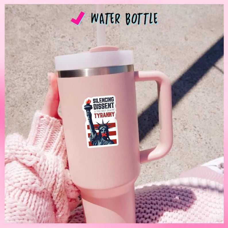 May include: A pink water bottle with a white lid and handle. A sticker on the bottle features the Statue of Liberty with a red band over its mouth and the text "Silencing Dissent is the First Sign of Tyranny."