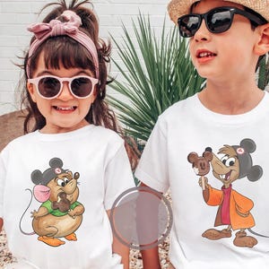 Puede incluir: Dos ni&ntilde;os con camisetas blancas con dibujos de ratones de dibujos animados. La ni&ntilde;a lleva gafas de sol rosas y una diadema a juego. El ni&ntilde;o lleva un sombrero de paja y gafas de sol. Ambas camisetas muestran un rat&oacute;n sosteniendo un helado de chocolate.