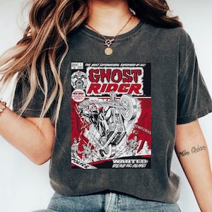 May include: A dark gray t-shirt with a vintage comic book design featuring Ghost Rider on a motorcycle. The comic book cover has red and black accents and the text "Ghost Rider" in bold white letters. The text "The Most Supernatural Superhero of All!" is printed above the title.