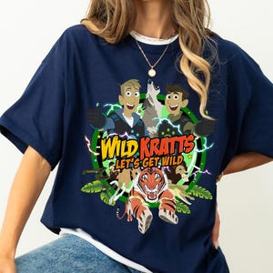 May include: A navy blue t-shirt with a graphic print of the Wild Kratts characters. The characters are surrounded by jungle animals and the text "Wild Kratts Let's Get Wild".