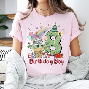 May include: Pink t-shirt with a green alien character wearing a birthday hat and holding a cone of ice cream. The number 8 is behind the alien and the text "8th Birthday Boy" is below the alien.