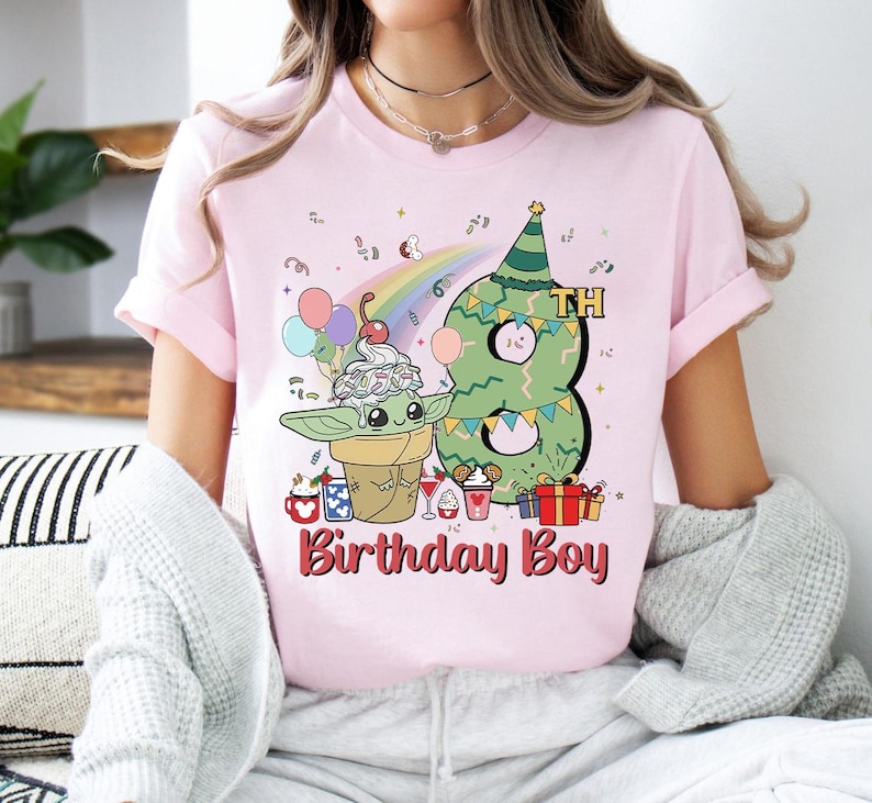 May include: Pink t-shirt with a green alien character wearing a birthday hat and holding a cone of ice cream. The number 8 is behind the alien and the text "8th Birthday Boy" is below the alien.