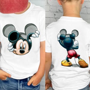 May include: White t-shirts featuring a Mickey Mouse graphic. One shirt shows Mickey's face, the other shows Mickey in a pose. The cartoon character is in black, blue, red, yellow, and white. The shirts are worn by a person.