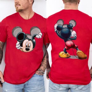 May include: Red t-shirt featuring a Mickey Mouse graphic on the front and back. The front graphic shows Mickey's face, while the back displays a full-body pose. The design includes black, white, yellow, and red colors.