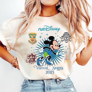 May include: Cream-colored t-shirt featuring Mickey Mouse running with a blue and green outfit. The shirt includes the text "runDisney Virtual Series 2025" with various Disney-themed graphics.