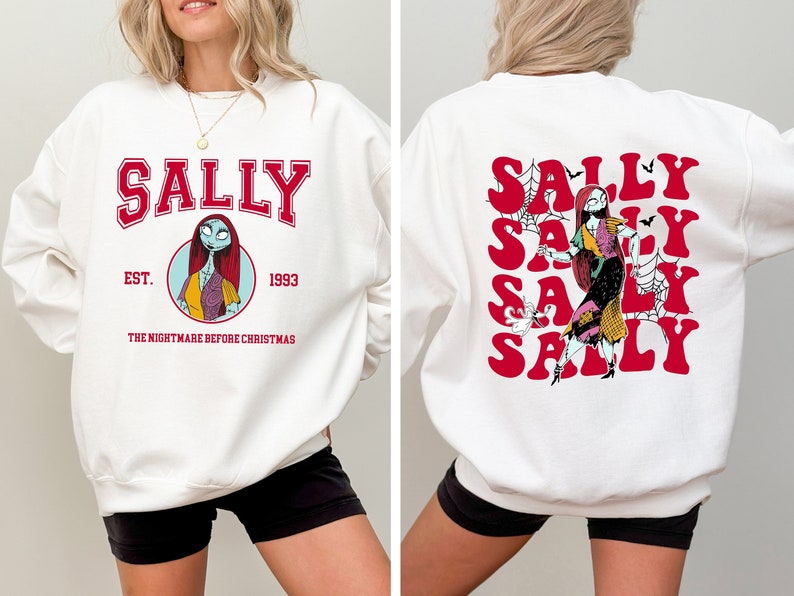 K&ouml;nnte beinhalten: Wei&szlig;er Pullover mit einem roten und schwarzen Aufdruck von Sally aus Nightmare Before Christmas. Die Vorderseite des Pullovers tr&auml;gt die Aufschrift "Sally Est. 1993 The Nightmare Before Christmas". Die R&uuml;ckseite des Pullovers zeigt das Wort "Sally" viermal in einer roten Retro-Schrift.