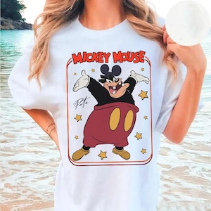 May include: White t-shirt featuring a cartoon image of Pete from Mickey Mouse. The graphic includes the text "Mickey Mouse" in red and Pete in a red and black outfit with yellow shoes. The design is framed by yellow stars.