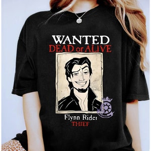 Puede incluir: Una camiseta negra con un diseño de cartel de se busca con una imagen de dibujos animados de Flynn Rider de la película Enredados. El cartel dice "WANTED DEAD or ALIVE" y "Flynn Rider THIEF".