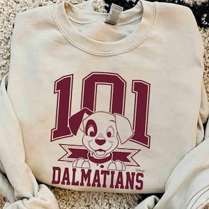 Puede incluir: Una sudadera beige con un gráfico marrón de un cachorro dálmata y el texto "101 Dálmatas".